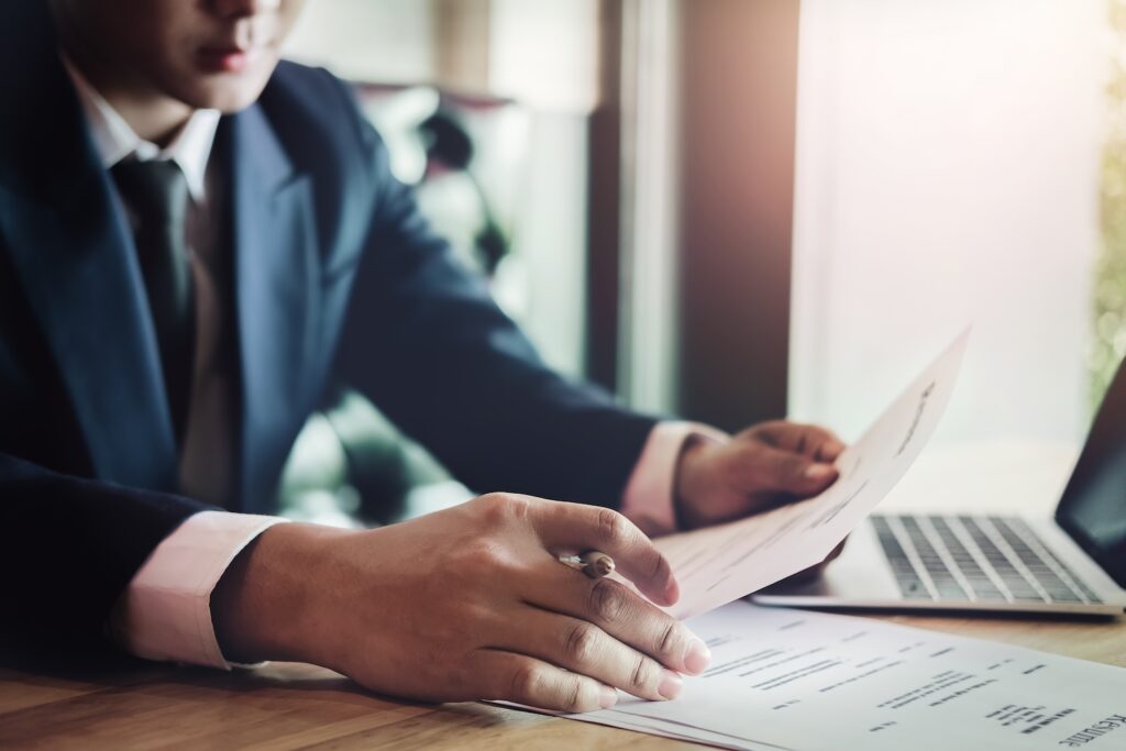 Business man reading agreement paper before sign document with use pen and laptop at work.